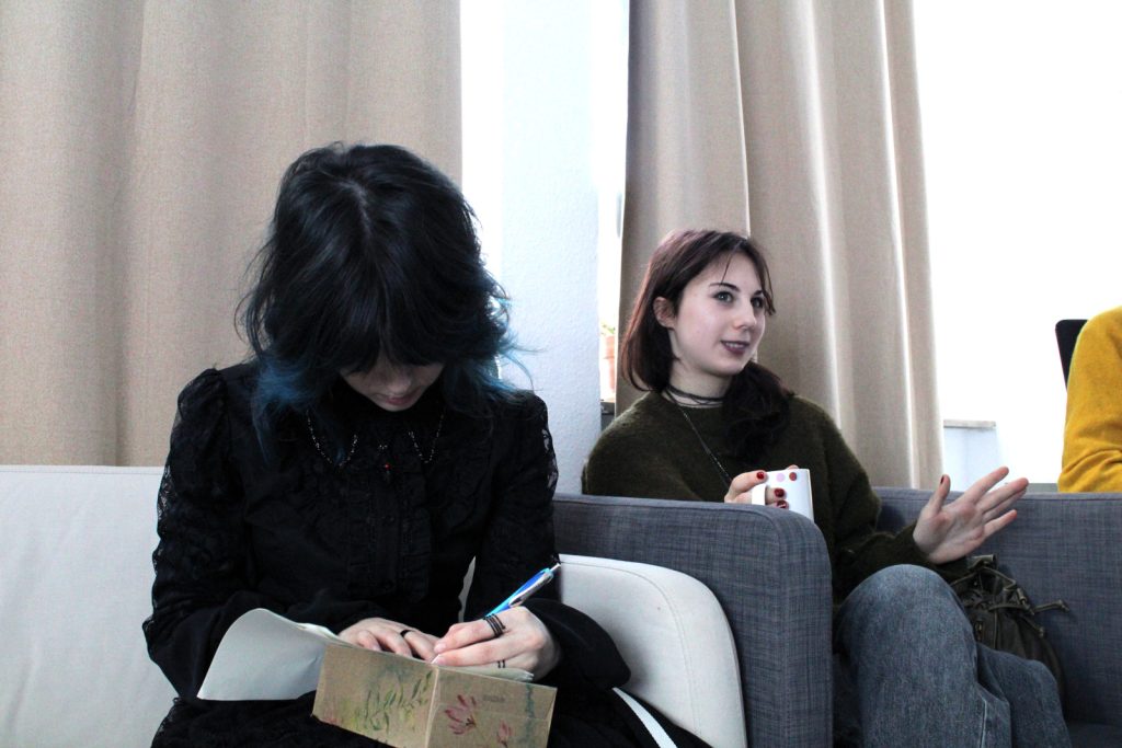 Teilnehmende des Debattierclubs im Austausch, eine Person macht sich Notizen während der Diskussion